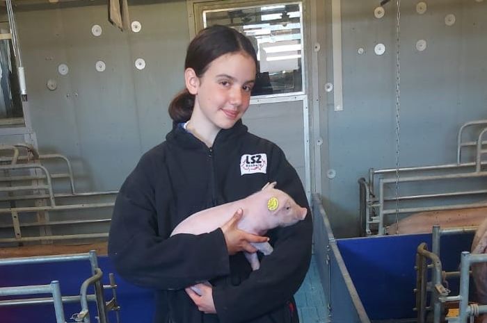 Eine Schülerin hält ein kleines Ferkel auf dem Arm.